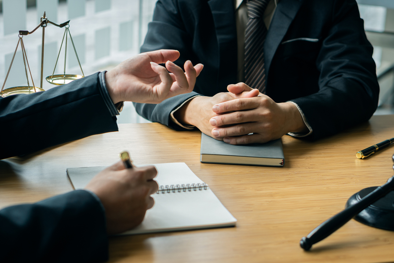 A male lawyer consults a team of legal clients and businessmen who are negotiating contracts. Human hands work with papers at the desk and sign contracts.Keywords: on the table with hammer and scales